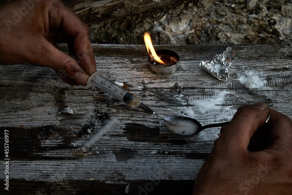 Obraz An addict prepares a dose of drugs. A syringe with a dose in your hand prepared on a spoon. The concept of drug addiction, the use of prohibited substances and drugs.