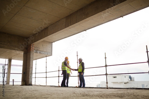 Obraz Construction workers handshaking at highrise construction site