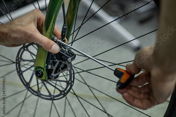 Obraz Cropped shot of professional mechanic working in bicycle repair shop, worker repairing bike using special tool
