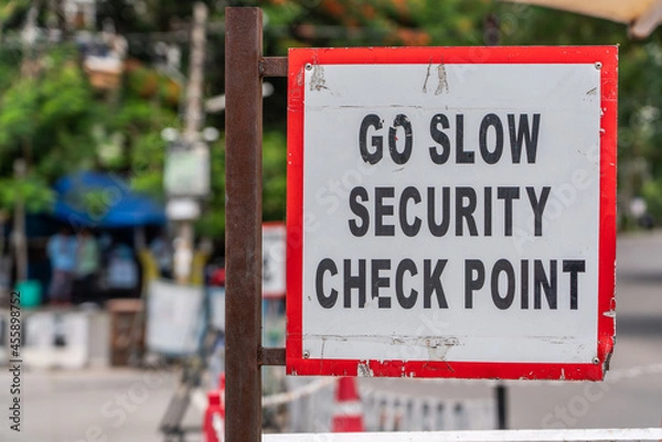 Fototapeta warning sign: "GO SLOW SECURITY CHECK POINT" with red frame, black letters on white background somewhere in a city 
