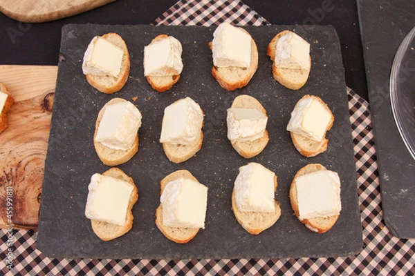 Fototapeta Slate table with small slices of bread and slices of cheese to taste