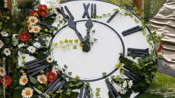 Fototapeta Large wall clock on the field in blooming flowers, showing the time 11:55, 12:00. time management concept, daylight saving time. Spring or wedding. Picnic for womens day