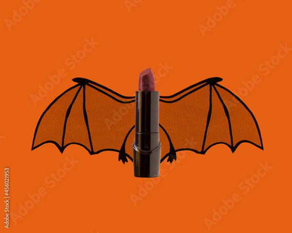 Fototapeta Dark red lipstick with bat wings on orange background for Halloween spooky beauty concept