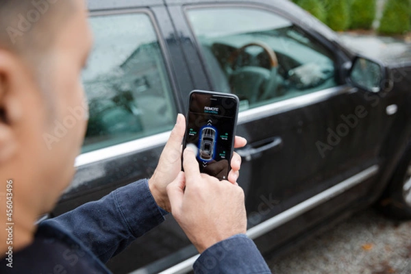 Obraz Man setting car alarm from smart phone in driveway