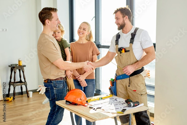 Fototapeta Builder Repairman In Overall Working Uniform Shake Hand To Clients Family After Agreement, After Sharing Ideas Of House Planning, Home Improvement. Side View