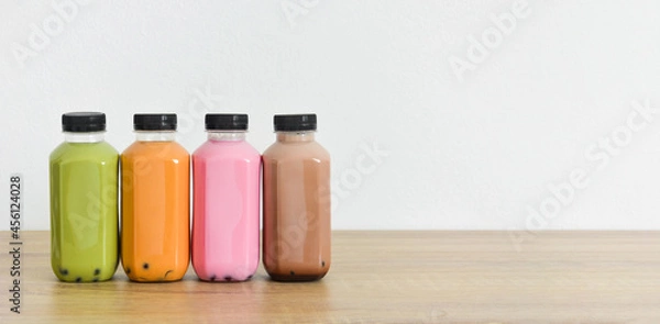 Fototapeta A row of various bobble tea in a plastic bottles on wooden table with white color background, copy space