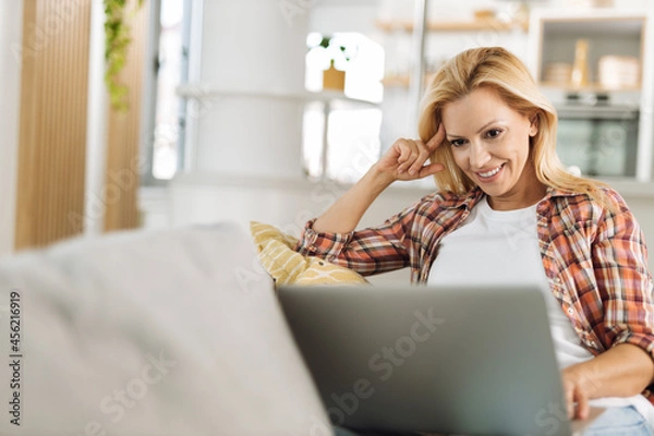 Fototapeta Young woman relaxing on sofa at home while using computer