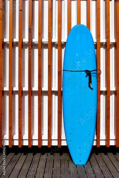 Obraz Blue surfboard leaning against a wall with wooden slats. Somewhere on a beach on the Madeira islands, Portugal. Beach and summer vibes.
