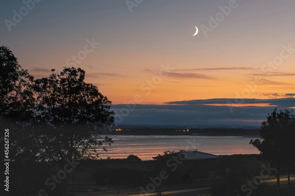 Fototapeta Waxing crescent moon over the sea at Sandwich bay during the golden hour sunset.