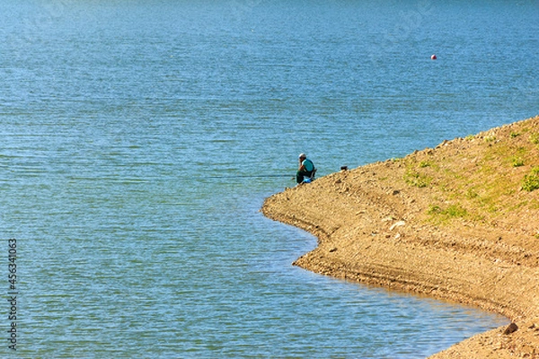 Obraz Lonely fisherman on the beach, in blue water background. Copy space