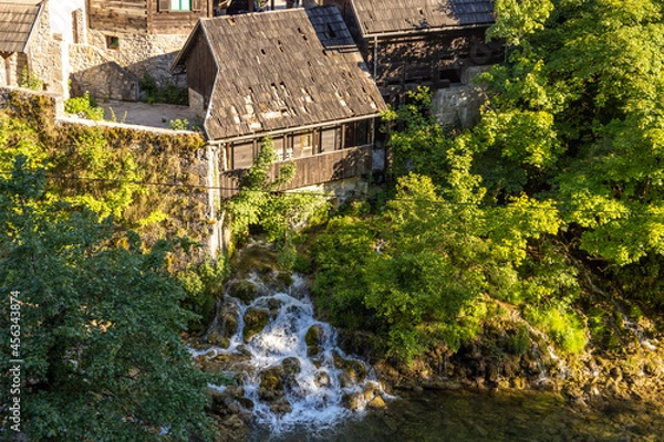 Obraz Old mill house on a small hill with waterfalls below and many trees.
