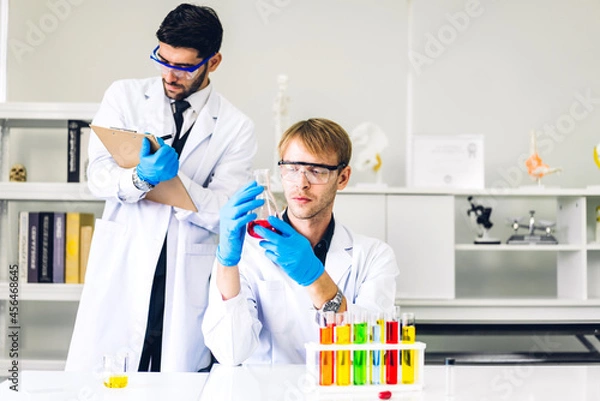 Obraz Professional two scientist man research and working doing a chemical experiment while making analyzing and mixing liquid in test tube.Young science man dropping sample chemical on glass at laboratory