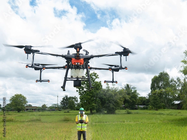Fototapeta Farmer technicians control agriculture drone fly to sprayed fertilizer on the green rice field smart farm. Agricultural technology concept.