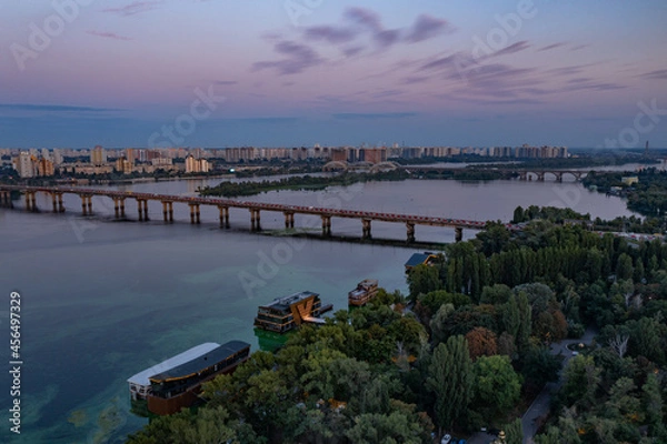 Fototapeta Evening Kiev from a bird's eye view. Architectural monuments. The light of lanterns and evening lights. City on the Dnieper. White buildings. Sunset.
