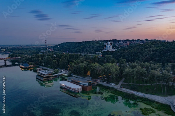 Fototapeta Evening Kiev from a bird's eye view. Architectural monuments. The light of lanterns and evening lights. City on the Dnieper. White buildings. Sunset.