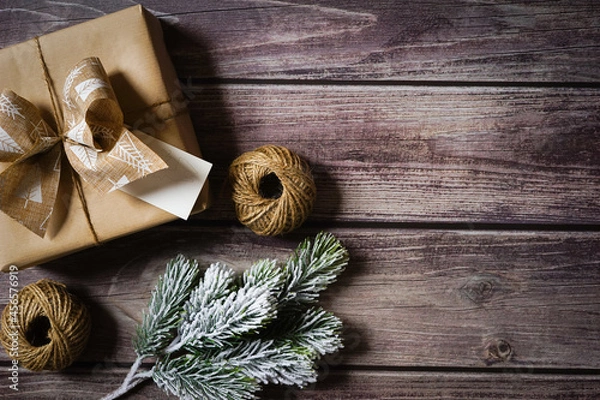 Fototapeta Christmas present wrapped in natural brown paper on wooden background. Festive holiday composition. Sustainable holiday gift wrapping concept. Gift giving. Empty space for text. Copy space.