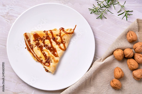 Obraz french crepes of cajeta (Dulce de leche) with walnuts on a white plate accompanied by walnuts on a brown cloth napkin. elegant concept. copy space for advertising.  top view