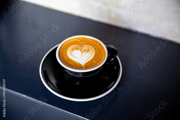 Fototapeta Black cup of cappuccino with latte art of heart shape on saucer on concrete background.