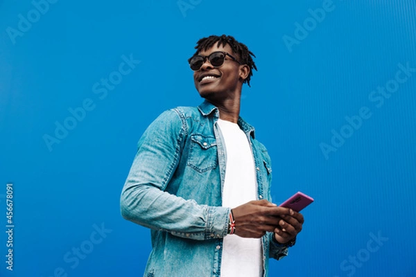 Fototapeta african man typing sms on blue background, 5g internet concept, high speed internet on phone
