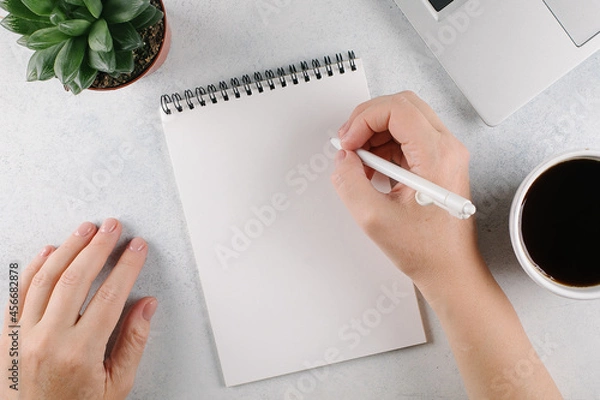 Fototapeta Womans hands writing to do list or plans in notebook on office desk. Top view, copy space