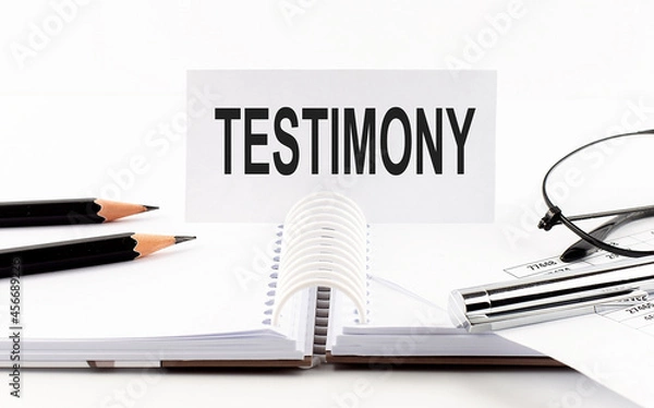 Fototapeta Text TESTIMONY on paper card,pen, pencils, glasses,financial documentation on table - business concept