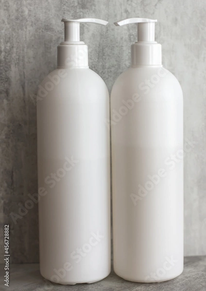 Obraz two empty white plastic containers with dispenser on a gray background. Minimalism.