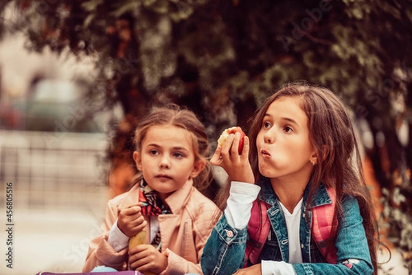 Obraz Two little girls on a school lunch break eat bananas and apples. Selective focus
