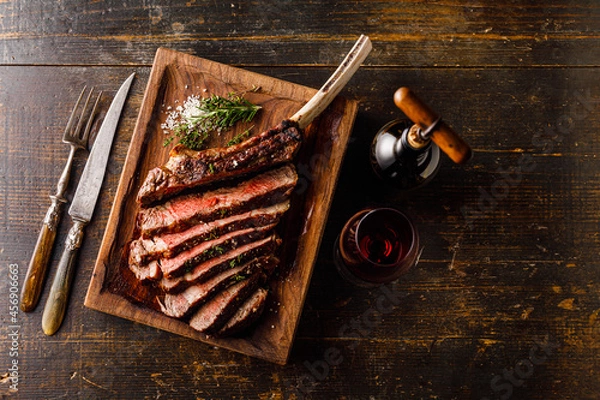Fototapeta Grilled sliced Tomahawk Steak on bone and glass of Red wine on wooden background