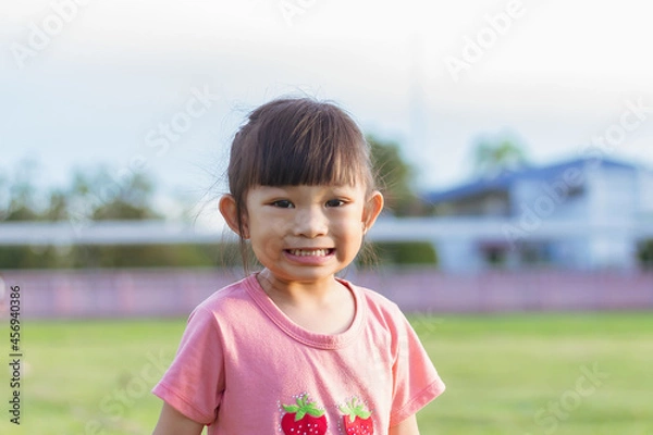 Fototapeta Portrait​ image of​ 3-4 years old​ baby​ child. Face of smiling​ Asian​ girl in head shot. Happy​ kid playing​ at the park playground. In summer or spring​ season.