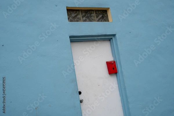 Obraz Closeup view at angle of blue painted building exterior with door and red mailbox, small glass window above. 