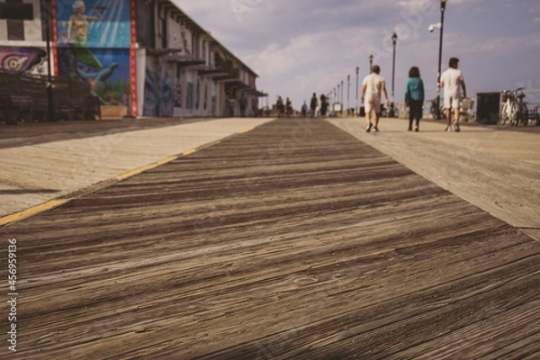 Obraz Long angle view of beach boardwalk, buildings and people walking in distance. 