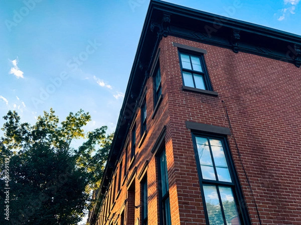 Obraz Looking up angled view of block of brownstone row home buildings with trees aligned left. 