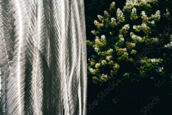 Obraz Side by side shot of metallic wall surface in focus foreground, flowering tree to right in background, slightly blurry. 