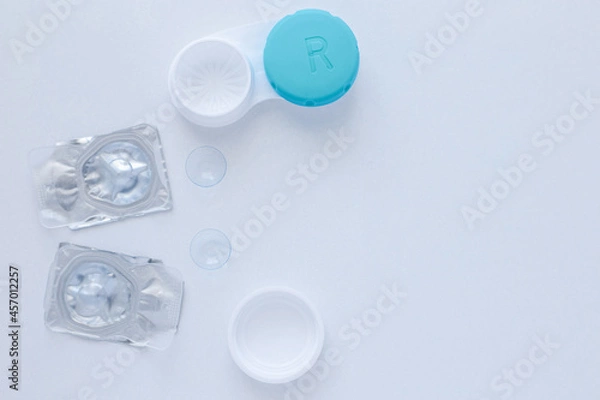 Fototapeta A container for lenses, two sealed lenses and lenses lying on a table on the side on a white background with a place for text. top view, flat lay, copy space, isolate