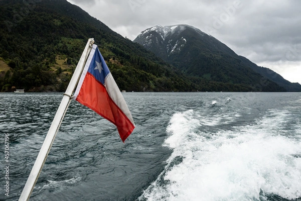 Fototapeta Chilean flag waving with in the Lago de Todos Los Santos and its snow-capped mountains in the background.