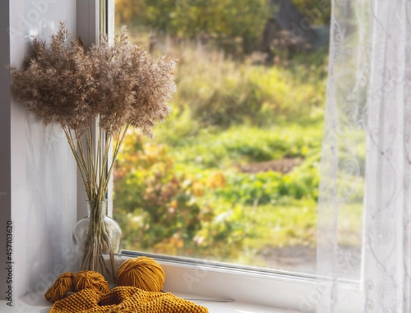 Fototapeta On the window the process of knitting and a bouquet of dry branches of grass. The concept of autumn and needlework.