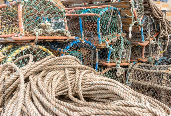 Fototapeta Bundle of nautical ropes and old lobster pots on the quayside of fishing port.