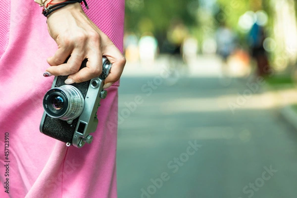 Fototapeta A young girl with a camera walks in a city park.