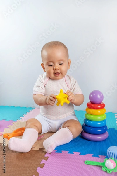 Fototapeta Happy toddler child playing with yellow rubber toy on colorful puzzle mat