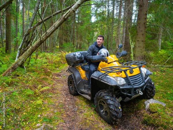 Fototapeta Man on a quad bike. ATV driver in the forest. A portrait of an quad bike driver. Concept - riding an ATV. Active rest of the quad bike. Riding a quad bike off-road. Man on yellow ATV