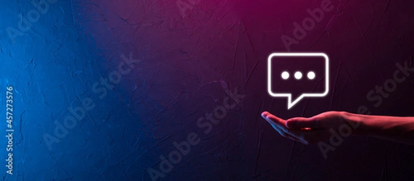 Fototapeta Hand on neon background holding a message icon, bubble talk notification sign in his hands. Chat icon, sms icon, comments icon, speech bubbles