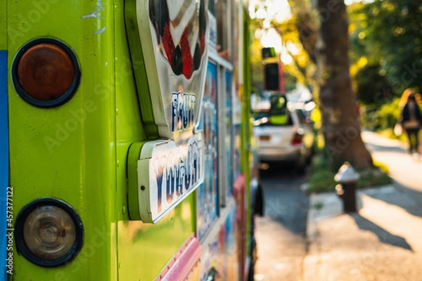 Obraz Rear left view of green ice cream truck, next to a park at sunset. 