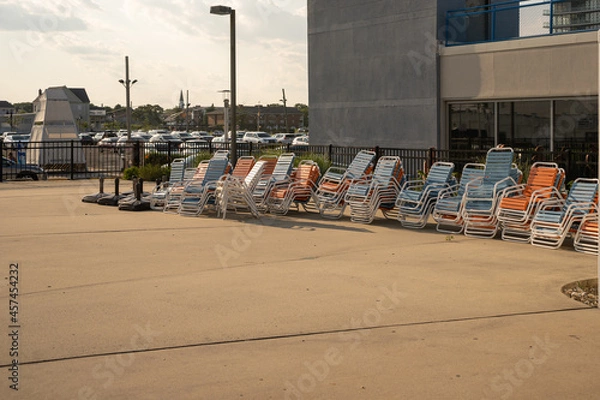 Obraz Stacked pool chairs, background against parking lot, concrete in foreground with copy space. 
