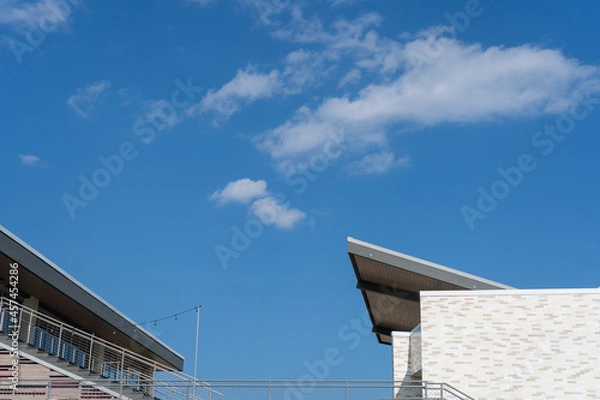 Obraz Looking up angle of building tops, cantilever roof angled with sky above. 