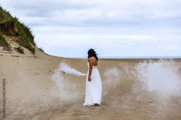 Fototapeta Junge schöne Frau im Hochzeitskleid am Strand mit einer Rauchfackel und weißen Rauch