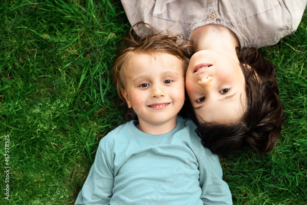 Obraz Portrait of two brothers lying on a grass in a park. Smiling happy children outdoors. Siblings friendship.
