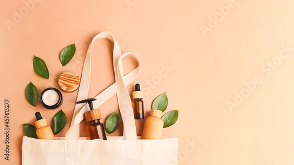 Fototapeta Open eco friendly cotton reusable bag with different containers from natural wood and brown glass.Fresh leafs around.Concept of organic,zero waste cosmetics.Woman bag with accessories,large banner.