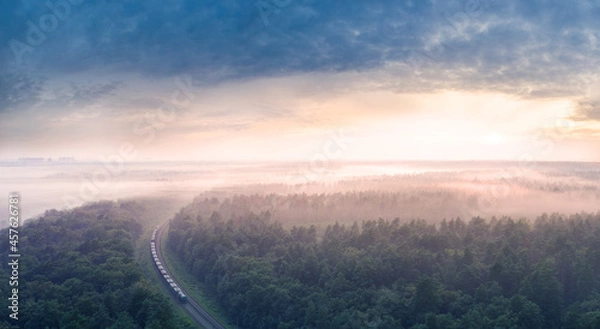 Fototapeta Dawn over the forest through which the railway line runs.