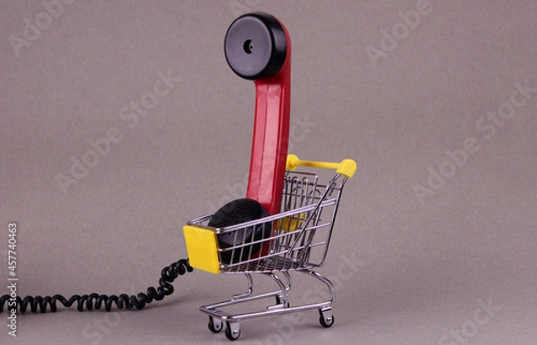 Fototapeta Red receiver from old rotary telephone in small shopping cart on gray background