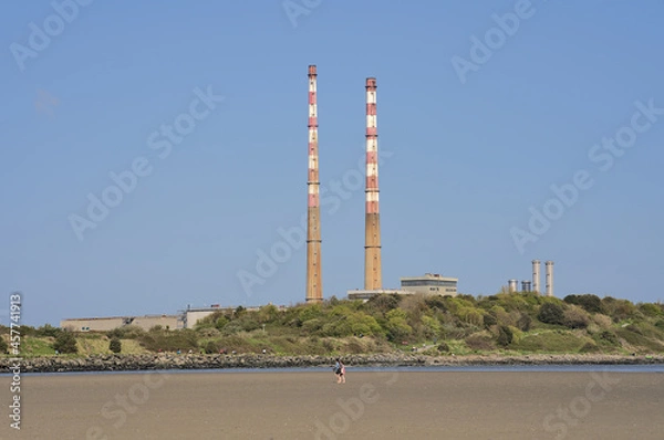 Fototapeta Beautiful closeup bright view of iconic Poolbeg power station chimneys and Poolbeg CCGT station against clear blue sky seen from Sandymount Beach, Dublin, Ireland. Soft colors. Copy space